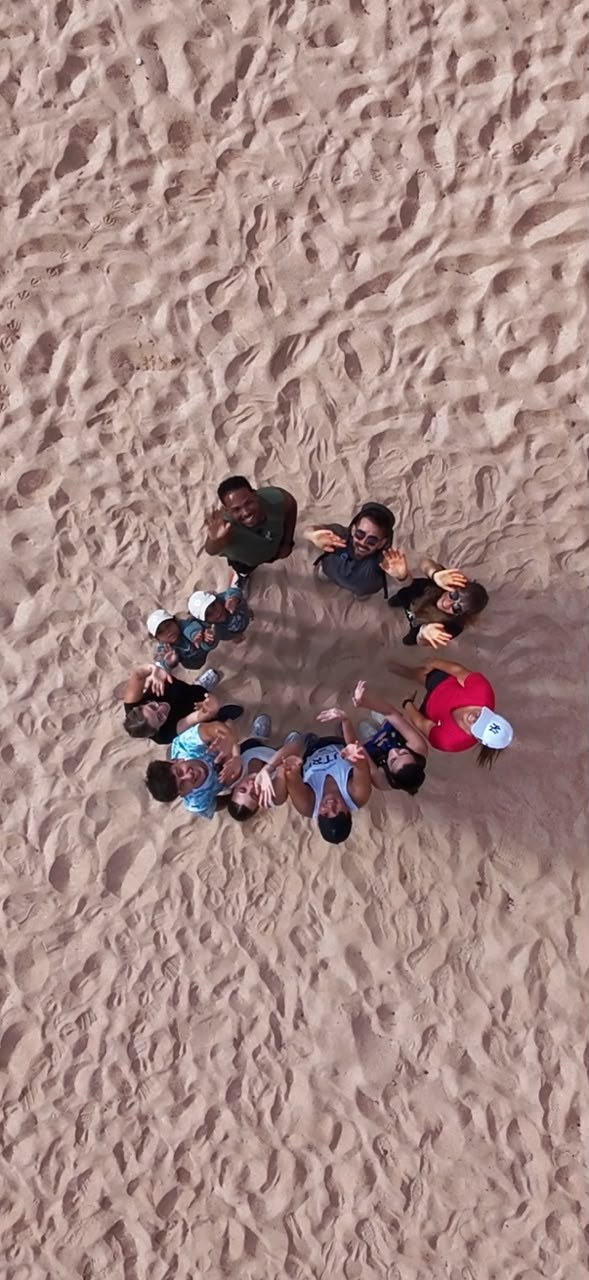 O grupo do Mindwalk em círculo na areia, visto de cima por um drone, a acenar