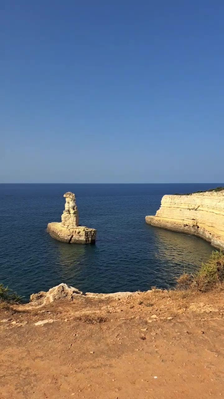 Rocha isolada no mar ao lado de falésias douradas